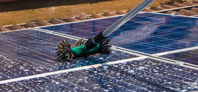 Een persoon reinigt zonnepanelen met een tuinslang.